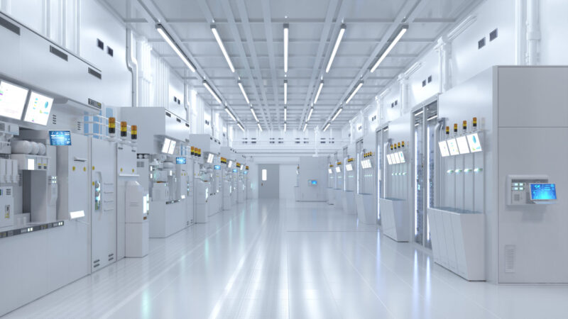 A modern, high-tech cleanroom designed to cGMP standards features bright lighting, white walls, and advanced machinery lining both sides, creating a sterile and futuristic environment typical of semiconductor or pharmaceutical manufacturing.