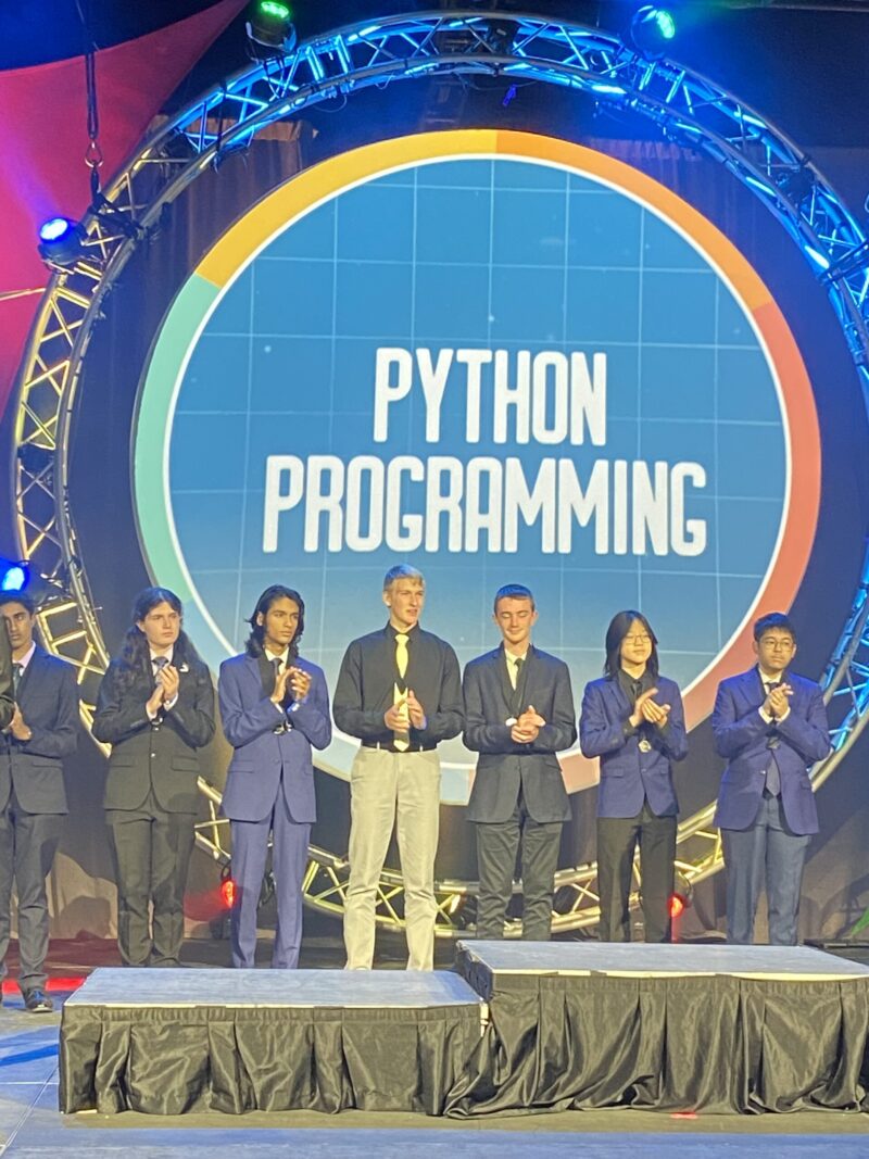 A group of people in formal attire stand on a stage in front of a large 