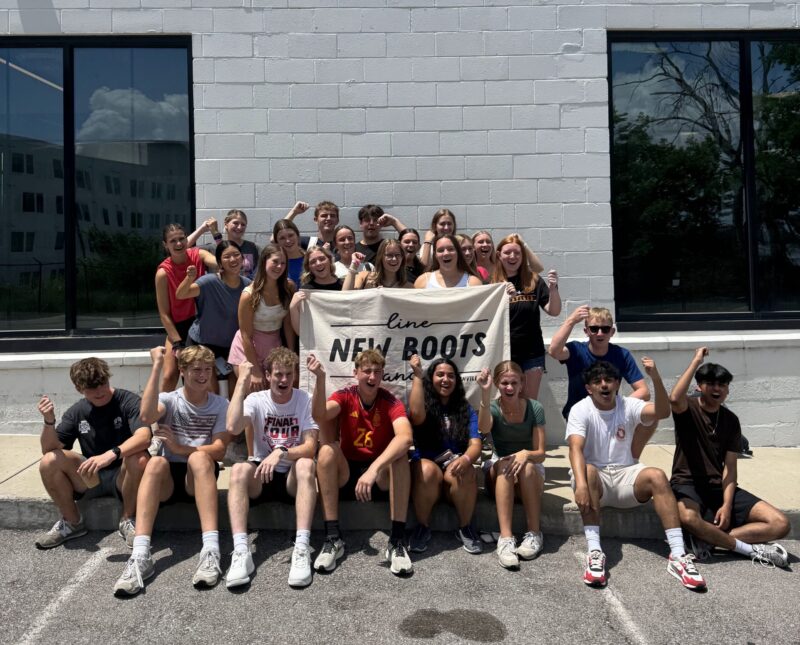 A group of young people from Butler Tech gather outside, smiling and cheering, while holding a 