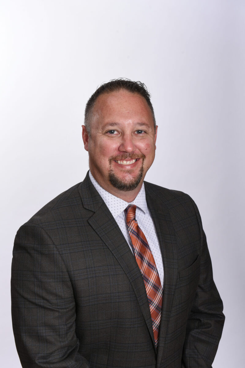 Tony Huff, sporting a plaid suit jacket, white shirt, and red-striped tie, smiles confidently against a light background—a proud advocate of CTE for All and recipient of a National Award.