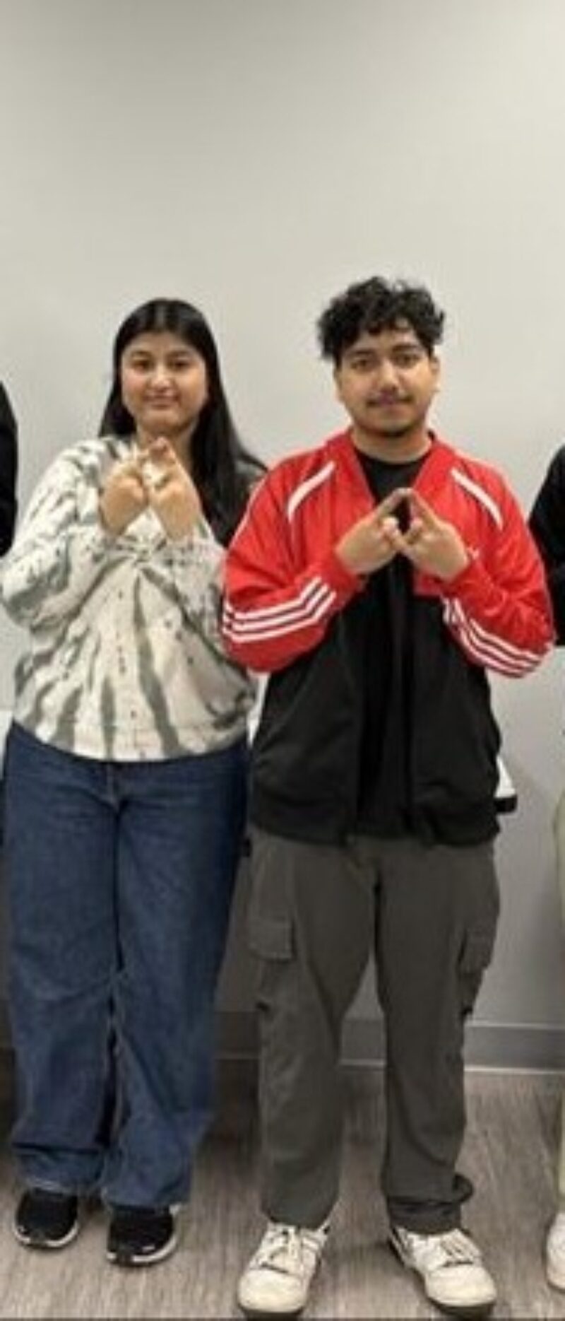 Two people stand side by side indoors against a plain wall, dressed casually—perfect for business students preparing for a DECA chapter startup challenge. Both hold their hands together in front, ready to take on new opportunities.