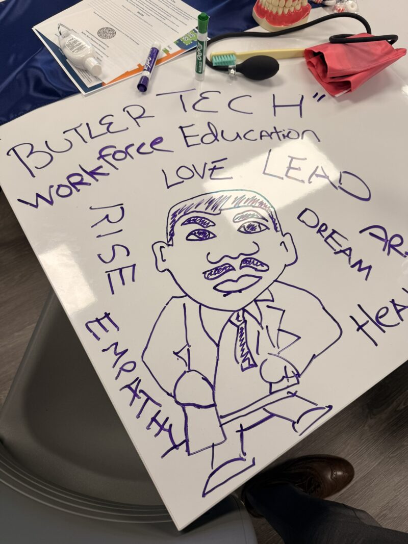 A whiteboard with a drawing of a man in a suit is surrounded by words like 