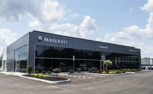 A modern black building with large windows houses a Maserati and Alfa Romeo dealership, labeled "Maserati Cincinnati," offering a premium automotive experience amid landscaped grounds and a spacious parking lot under a partly cloudy sky.