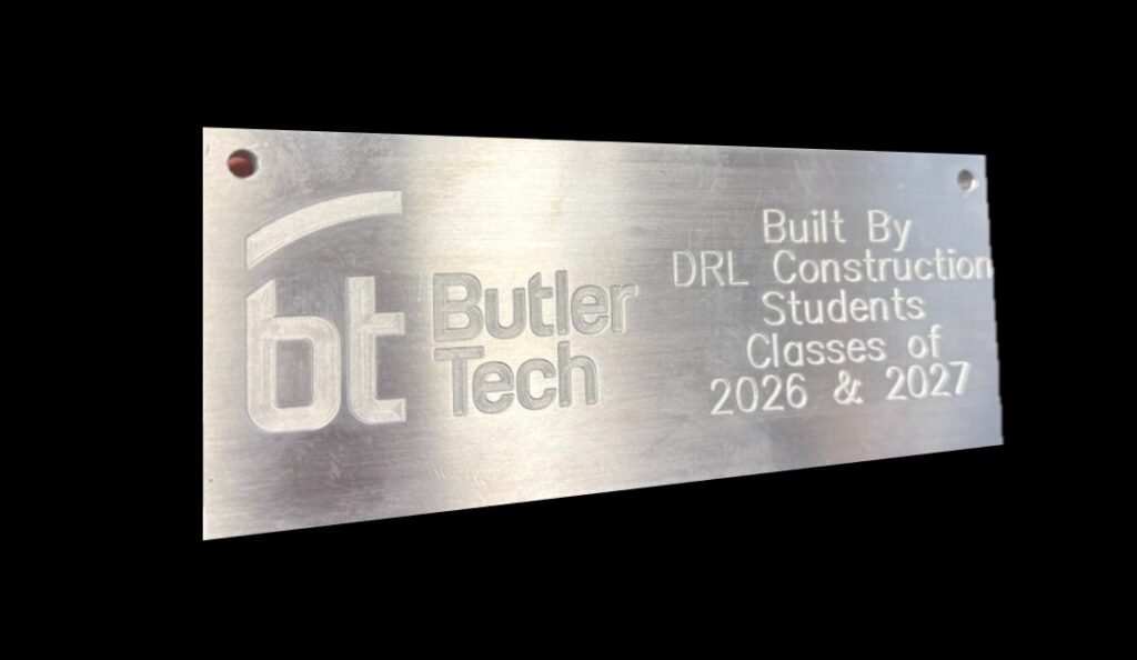 A metal plaque engraved with the Butler Tech logo and text: "Built By DRL Construction Students Classes of 2026 & 2027." The plaque celebrates construction education and has two holes for mounting on the left side.