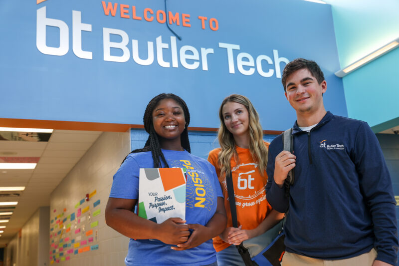 Three Student Ambassadors stand smiling under a 