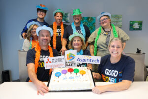 Eight smiling people in colorful hats and boas pose with a decorated cake that says “We did it!” Three sponsor logos are displayed above the cake, including LIFE Link. The group appears to be celebrating together in an office setting, highlighting their strong network and teamwork on Project LIFE.