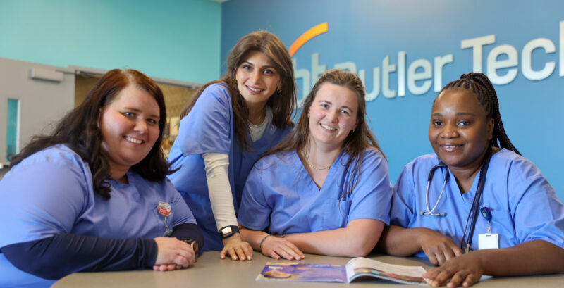 Four Butler Tech Adult Education Medical Assisting healthcare students in blue scrubs sitting at a round table with a brochure.