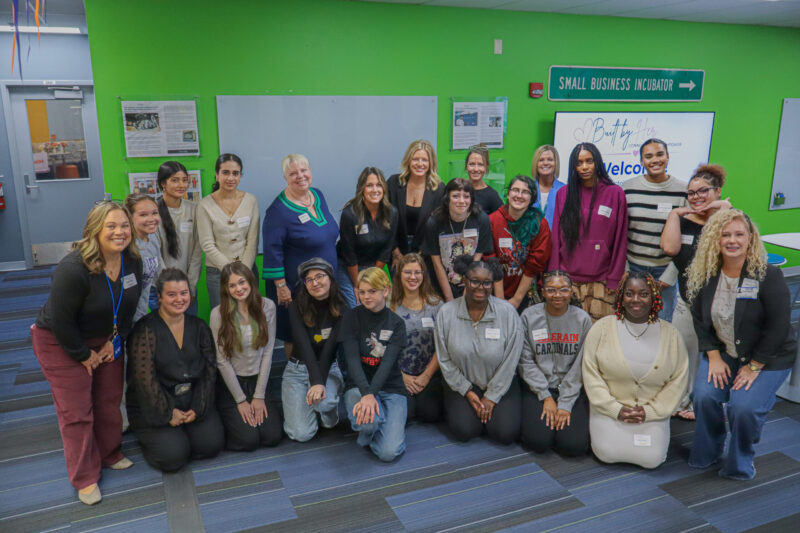 A large group of women leaders posing for a photo in a room with bright green walls and a “Small Business Incubator” sign.
