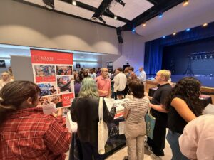 People gather around a Miami University booth at a career fair, talking with representatives. Brochures and posters highlight SOA students and professional skills, while a stage with blue lighting is visible in the background.